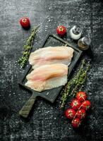 Fish fillet on a cutting Board with thyme, spices and tomatoes on a branch. photo