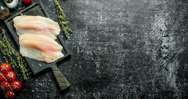 Fish fillet on a cutting Board with thyme, spices and tomatoes on a branch. photo