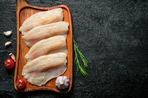 Fish fillet on a cutting Board with rosemary, garlic and tomatoes. photo