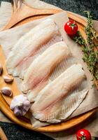 Tilapia fish fillet on a cutting Board with garlic cloves, tomatoes and thyme. photo