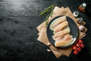 Tilapia fish fillet on a plate with paper, spices, thyme and tomatoes. photo