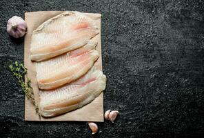Fish fillet on paper with thyme and garlic cloves. photo