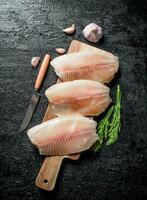Fish fillet on a cutting Board with a knife, dill and garlic. photo