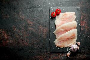 pescado filete en papel en un Roca tablero con ajo y Tomates. foto