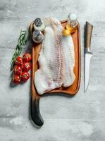 Fish fillet on a cutting Board with a knife, spices, oil and tomatoes on a branch. photo