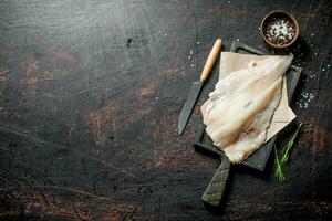 Fish fillet on cutting Board with knife, lemon slices and spices in bowl. photo