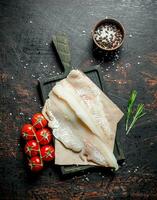 Fish fillets on the paper with a knife, rosemary and spices in a bowl. photo