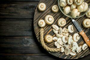 Mushrooms in a bowl and pieces of mushrooms on a tray with a knife. photo