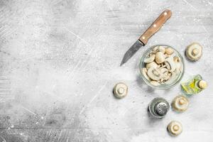 Sliced mushrooms in bowl with oil, pepper and knife. photo