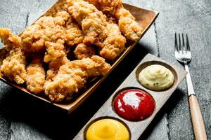 Chicken strips on a plate with different sauces and fork. photo