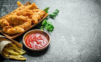 pollo tiras con perejil, francés papas fritas y tomate salsa en bol. foto