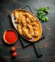 Chicken strips on a cutting Board with parsley and tomato sauce in a bowl. photo