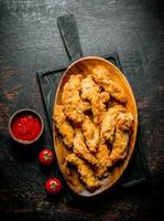 Chicken strips in a plate on a cutting Board with sauce and tomatoes. photo