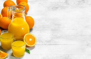 Orange juice in glass pitcher and fresh oranges. photo