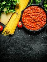 Bolognese sauce in pan with dry pasta, herbs and Parmesan. photo