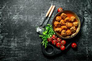 Meat balls in pan on a cutting Board with tomatoes and parsley. photo