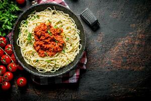 Spaghetti with Bolognese sauce in pan on a napkin with tomatoes and parsley. photo
