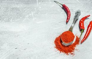 Ground red pepper in a spoon with fresh pepper pods. photo