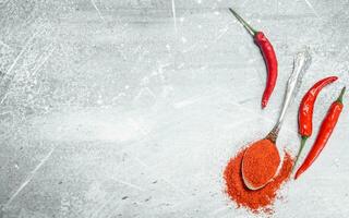 Ground red pepper in a spoon with fresh pepper pods. photo