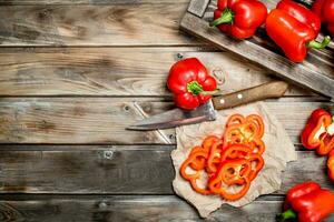 Rings of sweet pepper on paper with a knife and a whole pepper on tray. photo