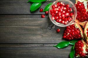 Pomegranate seeds in a bowl and pieces of ripe pomegranate with leaves. photo