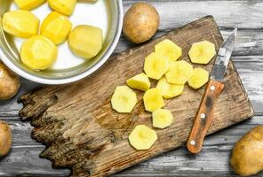 Sliced potatoes on a cutting Board with a knife and peeled potatoes in a saucepan. photo