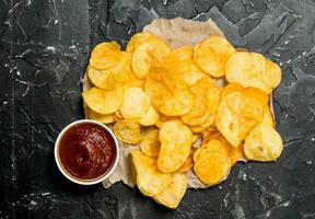Potato chips on old paper with tomato sauce. photo