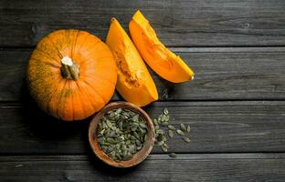 Pumpkin seeds in a bowl and pieces of ripe pumpkin. photo