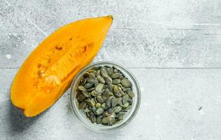 Pumpkin seeds in a bowl and a piece of ripe pumpkin. photo