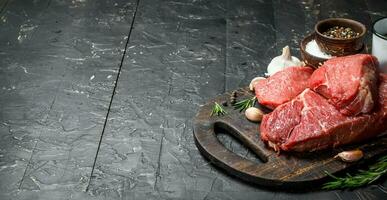 Raw meat. Pieces of beef with spices and herbs on a wooden Board. photo