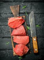 Raw meat. Pieces of beef with hatchet and rosemary branches. photo