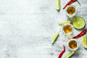 Tequila in a shot glass with slices of lime and red hot pepper. photo