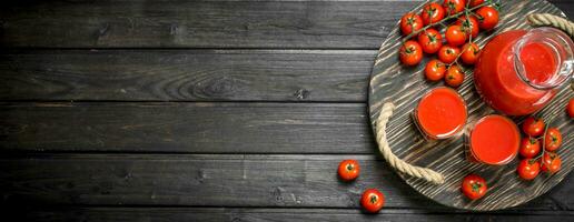 Tomato juice in a jug on the tray with tomatoes on a branch. photo