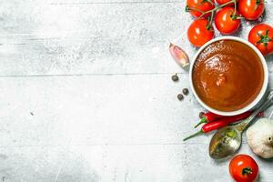 Tomato sauce in bowl with spoon, garlic and cherry. photo