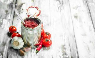 Tomato sauce in a tin can with a spoon and tomatoes. photo