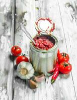 Tomato sauce in a tin can with a spoon, garlic and pepper. photo