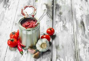 tomate salsa en un estaño lata con un cuchara, ajo y pimienta. foto