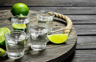 Vodka in a shot glass on a tray with slices of lime. photo