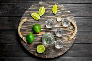 Vodka in a shot glass and a bottle on tray with lime. photo