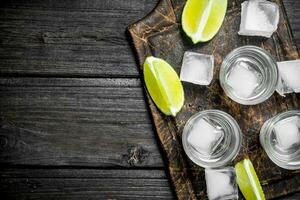 vodka con hielo en un corte tablero con rebanadas de Lima. foto