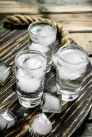 Vodka in a shot glass and ice cubes on tray. photo