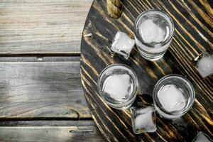 Vodka in a shot glass and ice cubes on tray. photo