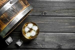 Whiskey in a glass with ice cubes and a barrel. photo