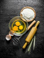 Flour with eggs, whisk and rolling pin. photo