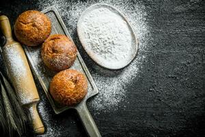 Crusty buns on a cutting Board with flour from the bowl. photo