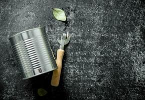 Closed tin can with a opener and a Bay leaf. photo