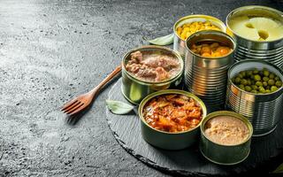 Various open tin cans of canned food on a stone Board with a fork. photo