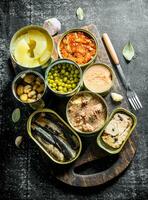Open tin cans with various canned food on wooden cutting Board. photo