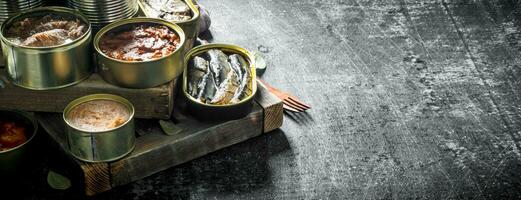 Various open tin cans with canned food on wooden tray. photo