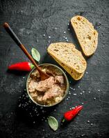 Open jar with canned meat with hot red pepper and bread. photo